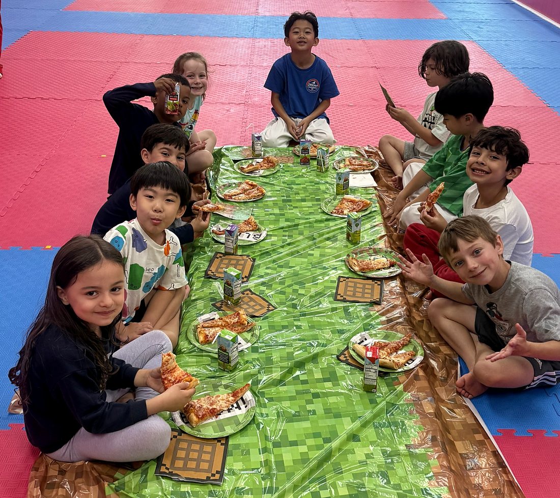 Kids enjoying pizza at a long party table on the mats